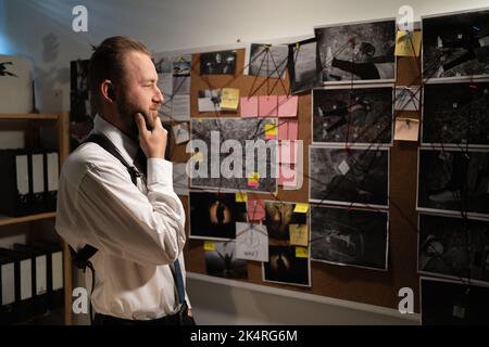 Polizist, der Informationen über Verbrechen auf der Untersuchungstafel analysiert, arbeitet in der Nacht im Büro Stockfoto