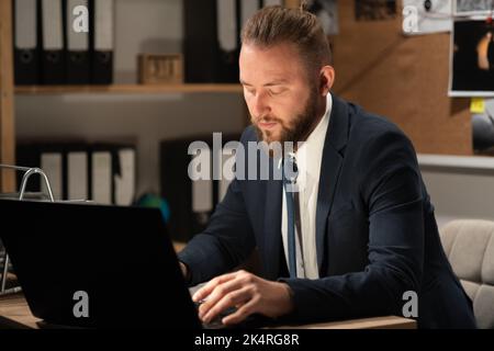 Detective verarbeitet Beweise im Büro, indem er nachts am Schreibtisch seines Büros einen Computer verwendet Stockfoto