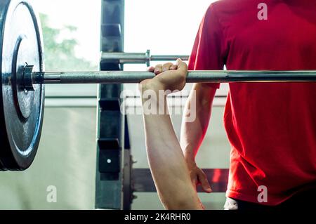 Person, die Brust-Übungen mit einer Langhantel in der Turnhalle. Die Couch steht neben ihm und kontrolliert die Übung. Stockfoto