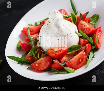 Salat mit Tomaten und Burrata-Käse mit Basilikum und Olivenöl auf dem Teller. Italienisches Essen. Stockfoto