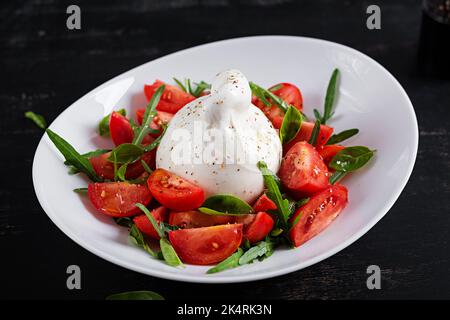Salat mit Tomaten und Burrata-Käse mit Basilikum und Olivenöl auf dem Teller. Italienisches Essen. Stockfoto