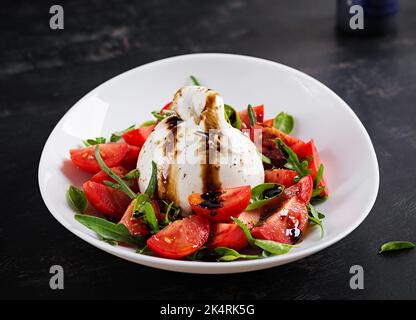 Salat mit Tomaten und Burrata-Käse mit Basilikum und Olivenöl auf dem Teller. Italienisches Essen. Stockfoto
