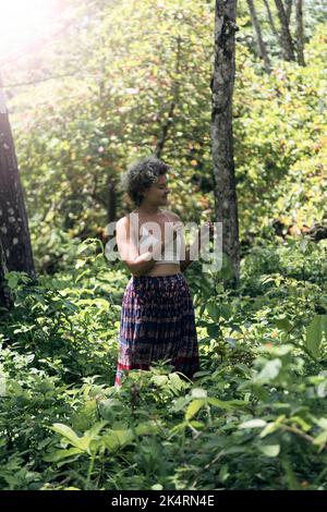 Kaukasische Frau mit blonden Haaren, gekleidet in ein weißes T-Shirt und einen langen Rock, der durch den Wald läuft. Sommerliche Stimmung Stockfoto