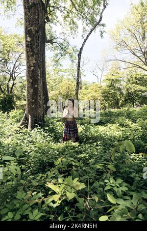 Kaukasische Frau mit blonden Haaren, gekleidet in ein weißes T-Shirt und einen langen Rock, der durch den Wald läuft. Sommerliche Stimmung Stockfoto