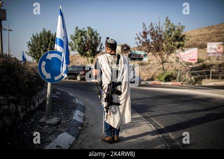 Nablus, Palästinensische Gebiete. 04. Oktober 2022. Ein israelischer rechter Siedler trägt eine Waffe am Haupteingang der palästinensischen Stadt Nablus im nördlichen Westjordanland, während israelische rechte Siedler beten. Quelle: Ilia Yefimovich/dpa/Alamy Live News Stockfoto