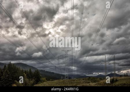 Hochspannungstürme mit Stromübertragungsleitungen im Land unter dunklen Wolken. Stockfoto