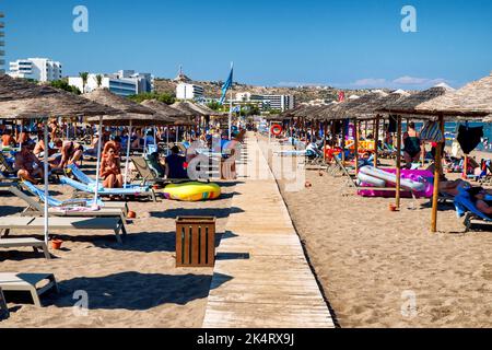 FALIRAKI, GRIECHENLAND - 29. JUN 2022: Menschen entspannen sich unter Sonnenschirmen am Sandstrand im Resort Faliraki auf der Insel Rhodos Stockfoto