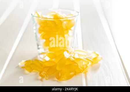 Fischöl-Kapseln. Gelbe Omega 3 Pillen im Glas auf dem weißen Tisch. Stockfoto