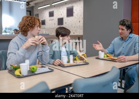 Die Schüler essen mit ihrem Lehrer in der Kantine zu Mittag Stockfoto