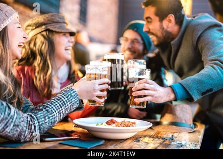 Freundliche Jungs, die sich im Winter im Bierlokal im Freien an glückliche Mädchen heranmachen - Freundschaftskonzept mit jungen Menschen, die gemeinsam Spaß am Trinken getrunken haben Stockfoto