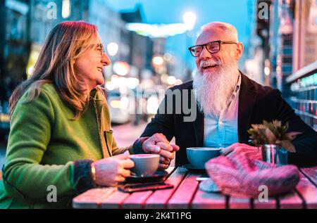Hipster Rentnerehepaar verliebt sich in Cappuccino in der Cafeteria im Freien - fröhliches, älteres Lifestyle-Konzept mit Frau und Mann, die Spaß daran haben Stockfoto