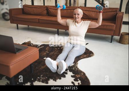 Fröhliche reife blonde Frau macht Kraft-Workout Stockfoto