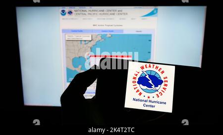 Person, die das Smartphone mit dem Logo der US-amerikanischen NWS-Division National-Windsurmzentrum (NHC) auf dem Bildschirm vor der Website hält. Konzentrieren Sie sich auf die Telefonanzeige. Stockfoto