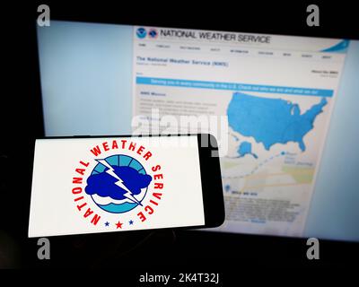 Person, die Mobiltelefon mit dem Logo der US-Agentur National Weather Service (NWS) auf dem Bildschirm vor der Webseite hält. Konzentrieren Sie sich auf die Telefonanzeige. Stockfoto