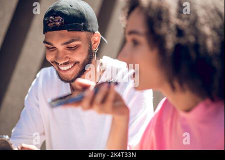 Nette junge Frau im rosa Hemd, die eine Sprachnachricht aufzeichnet Stockfoto