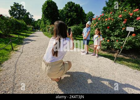 Mutter fotografiert Kinder im Garten mit ihrem Telefon. Stockfoto
