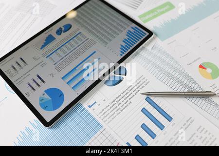 Auf statistischen Berichten liegt ein Tablet mit Diagrammen auf dem Bildschirm Stockfoto