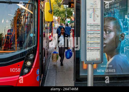 London, Großbritannien. September 29 2022 .Ein roter Doppeldeckerbus und eine Frau mit Einkaufstaschen an der Bushaltestelle in Lewisham. Stockfoto