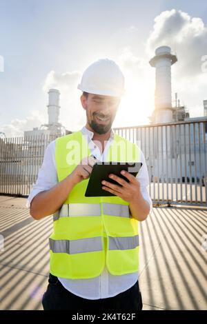 Vertikales Foto eines Ingenieurs aus dem Smiley-Kaukasus, der digitale Tablets zur Durchführung von Inspektionen im Energiewerk verwendet. Stockfoto