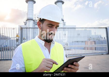 Nahaufnahme eines kaukasischen Ingenieurs, der bei einer Inspektion in einem thermoelektrischen Werk ein digitales Tablet verwendet. Arbeiter außerhalb des Kraftwerks. Stockfoto