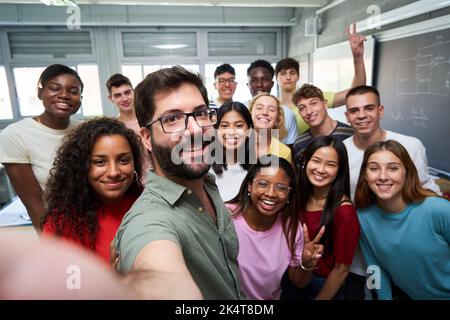 Glückliches Selfie einer jungen Gruppe von Erasmus-Studenten, die ein Foto mit ihrem Lehrer im Klassenzimmer machen. Stockfoto