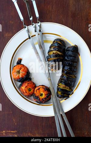 Geröstete Tomaten und Zucchini mit Metallspießen auf dem Teller Stockfoto