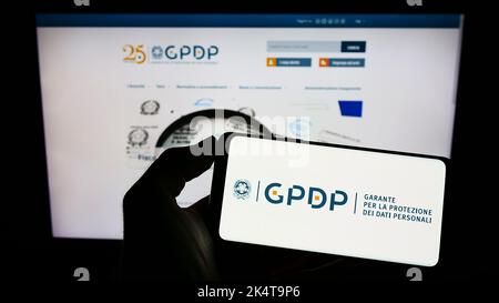 Person, die Mobiltelefon mit dem Logo der italienischen Datenschutzbehörde (GPDP) auf dem Bildschirm vor der Webseite hält. Konzentrieren Sie sich auf die Telefonanzeige. Stockfoto