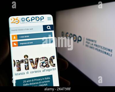 Person, die Mobiltelefon mit der Website der italienischen Datenschutzbehörde (GPDP) auf dem Bildschirm vor dem Logo hält. Konzentrieren Sie sich auf die Mitte des Telefondisplays. Stockfoto