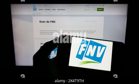 Person, die das Smartphone mit dem Logo der niederländischen Federatie Nederlandse Vakbeweging (FNV) auf dem Bildschirm vor der Website hält. Konzentrieren Sie sich auf die Telefonanzeige. Stockfoto