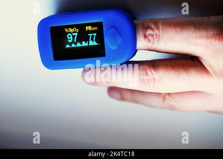 Hnad mit Pulsoximeter, das die Sättigung und den Puls des Patienten anzeigt Stockfoto