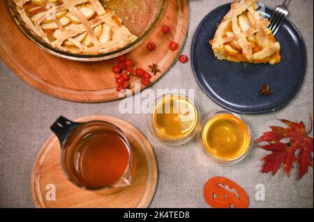 Stillleben. Frischer Kürbiskuchen mit knuspriger Kruste für Thanksgiving, Teekannen, zwei Tassen heißen Tee, umgeben von Ahornblättern Stockfoto