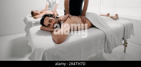 Mann und Frau genießen die Massage auf Massageliegen mit geschlossenen Augen. Schönes Paar während einer Rückenmassage, gemeinsamer Tag im Massagesalon Stockfoto