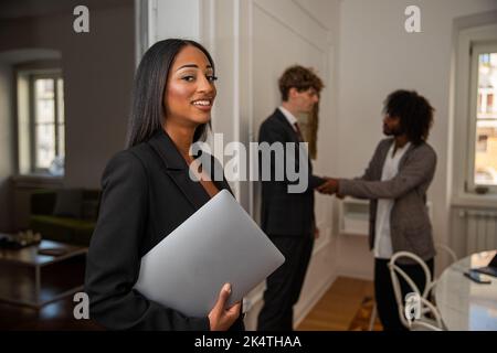 Geschäftsfrau im Büro mit ihrem Laptop, Kollegen im Hintergrund, die nicht fokussiert über Arbeits-, Unternehmens- und Bürokonzept diskutieren Stockfoto