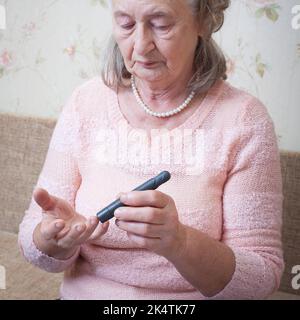 Ältere Frau, die den Blutzuckerspiegel mit Glucometer überprüft. Nahaufnahme einer alten Person mit Diabetes. Diabetesbehandlung für ältere Menschen. Stockfoto