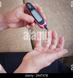 Ältere Frau, die den Blutzuckerspiegel mit Glucometer überprüft. Nahaufnahme der alten Person mit Diabetes. Diabetesbehandlung für ältere Menschen. Stockfoto