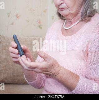 Ältere Frau, die den Blutzuckerspiegel mit Glucometer überprüft. Nahaufnahme einer alten Person mit Diabetes. Diabetesbehandlung für ältere Menschen. Stockfoto