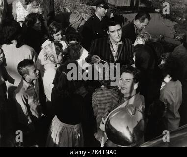 Elvis vor Ort am Lake Pontchartrain Shack, New Orleans, März 4,1958. Elvis signiert Autogramme für wartende Fans. Elvis trägt ein Hemd, das im Film nicht zu sehen ist, also kommt er entweder an oder verlässt den Ort. Stockfoto