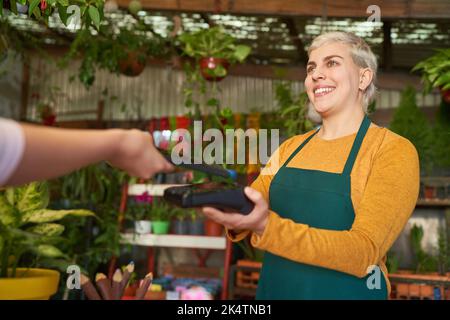 Kunde mit Smartphone-App zahlt kontaktlos am NFC-Kartenterminal im Blumenladen Stockfoto