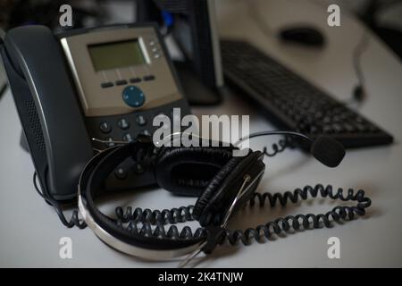 Stationäres Telefon und Headset auf dem Schreibtisch in Innenräumen, Nahaufnahme. Kommunikationsunterstützung, Call Center und Kundendienst. Stockfoto