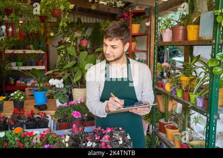 Junger Gärtner mit Clipboard, der Inventar- und Qualitätskontrolle im Blumenladen macht Stockfoto