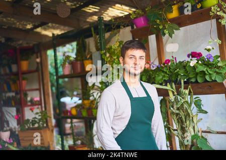 Junger Mann mit Schürze als Floristin oder Fachverkäufer im Baumschulgeschäft Stockfoto