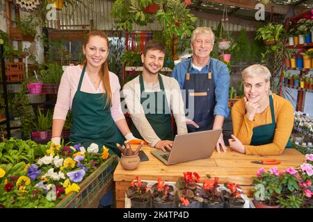 Freundliches Team von Gärtnern und Floristen am Laptop-Computer im Familienbetrieb Stockfoto