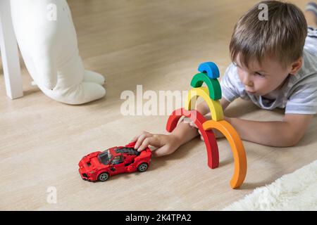 Lächelndes männliches Kind, das mit Montessori-Regenbogenblöcken aus Holzmaterial ein rotes Auto spielt Stockfoto