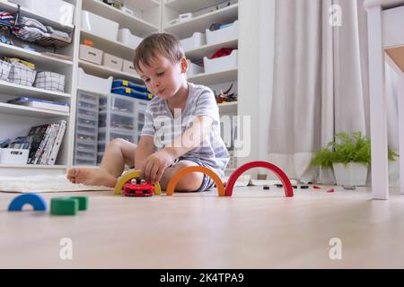 Lächelndes männliches Kind, das mit Montessori-Regenbogenblöcken aus Holzmaterial ein rotes Auto spielt Stockfoto