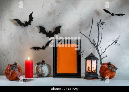 Hallowen festliche Komposition auf weißem Holztisch im texturierten Hintergrund. Dekorative Kürbisse, schwarzer Rahmen, Fledermäuse, Spinnen, brennende Kerze, Laterne, Cob Stockfoto