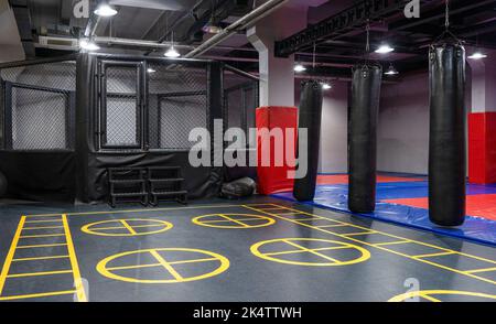 Ein achteckiger Kickboxen-Käfig mit Boxsäcken im Sportkomplex. Stockfoto