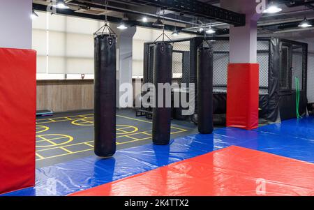 Ein achteckiger Kickboxen-Käfig mit Boxsäcken im Sportkomplex. Stockfoto