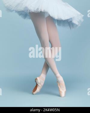 Beschnittenes Bild von weiblichen Beinen, Ballerina in Tutu und pointe auf Zehenspitzen isoliert über blauem Studiohintergrund stehend Stockfoto
