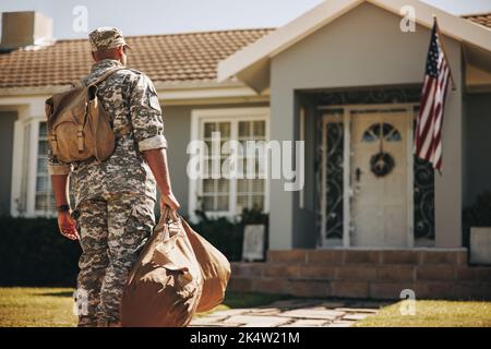 Rückansicht eines mutigen jungen Soldaten, der mit seinem Gepäck auf sein Haus zuläuft. Amerikanischer Militärangehöriger, der nach seinem Dienst in seinem Land nach Hause zurückkehrt Stockfoto