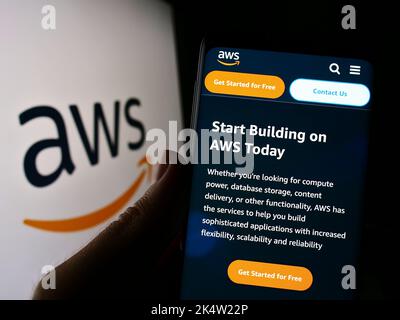 Person mit Mobiltelefon und Website des US-Cloud-Unternehmens Amazon Web Services Inc. (AWS) auf dem Bildschirm mit Logo. Konzentrieren Sie sich auf die Mitte des Telefondisplays. Stockfoto